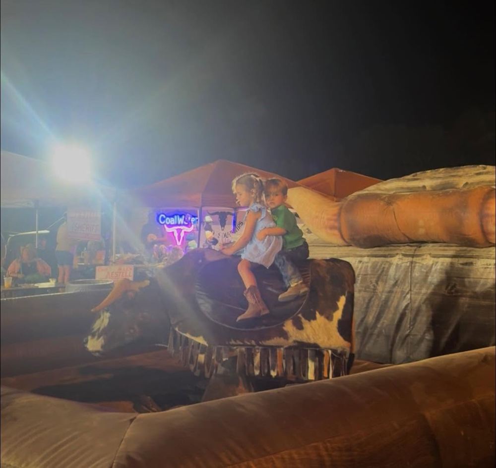 Two kids riding the mechanical bull together at a night event